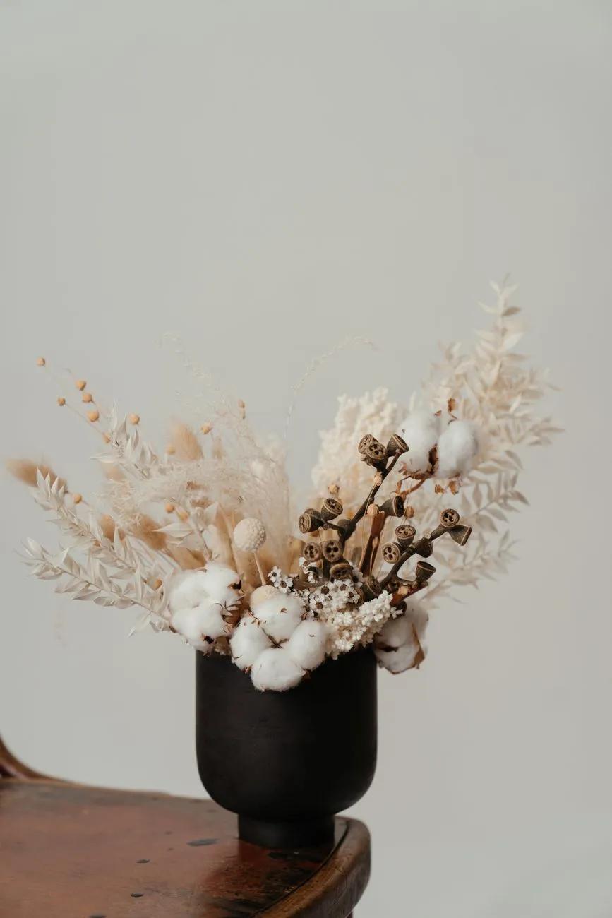 Bouquet de fleurs séchées avec coton dans un vase noir, posé sur une table en bois clair