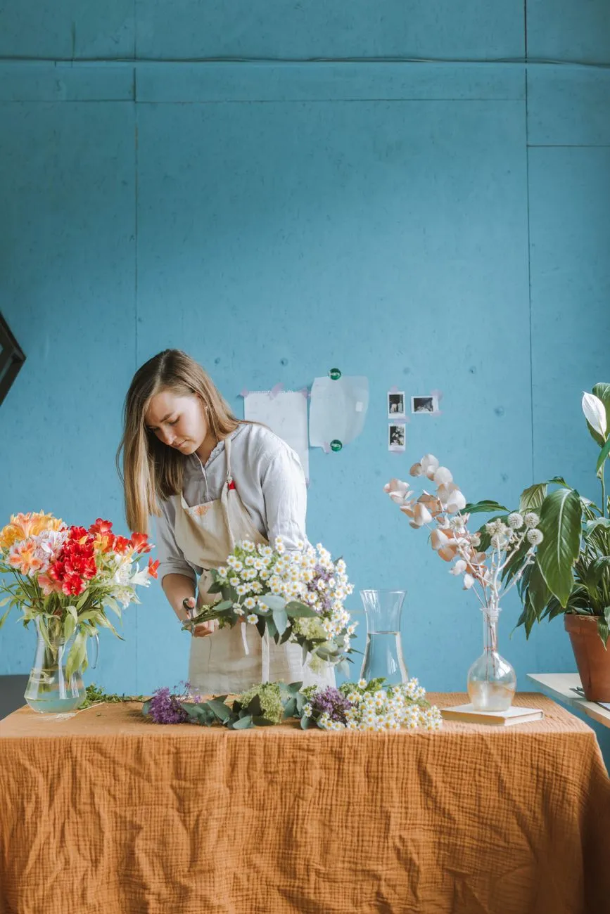 Fleuriste disposant des fleurs colorées autour d’une base ronde sur une table d’atelier lumineuse