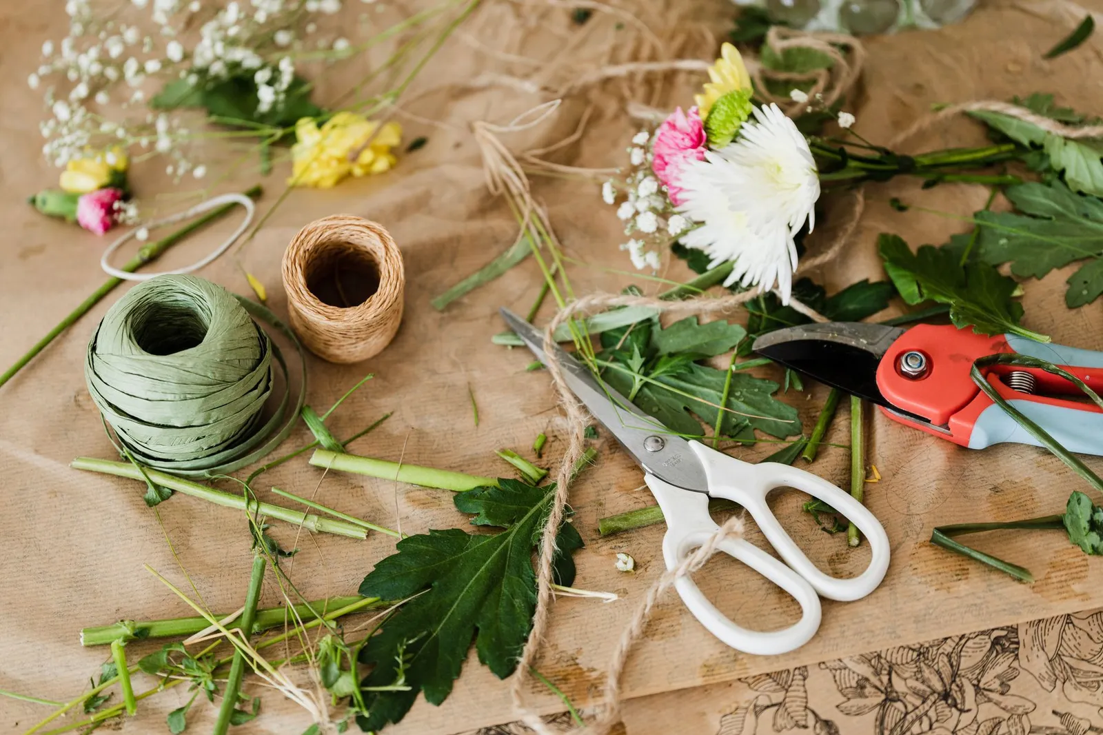 Vue de dessus d’un sécateur, de ficelle, de ciseaux et de fleurs dispersés sur un établi en bois