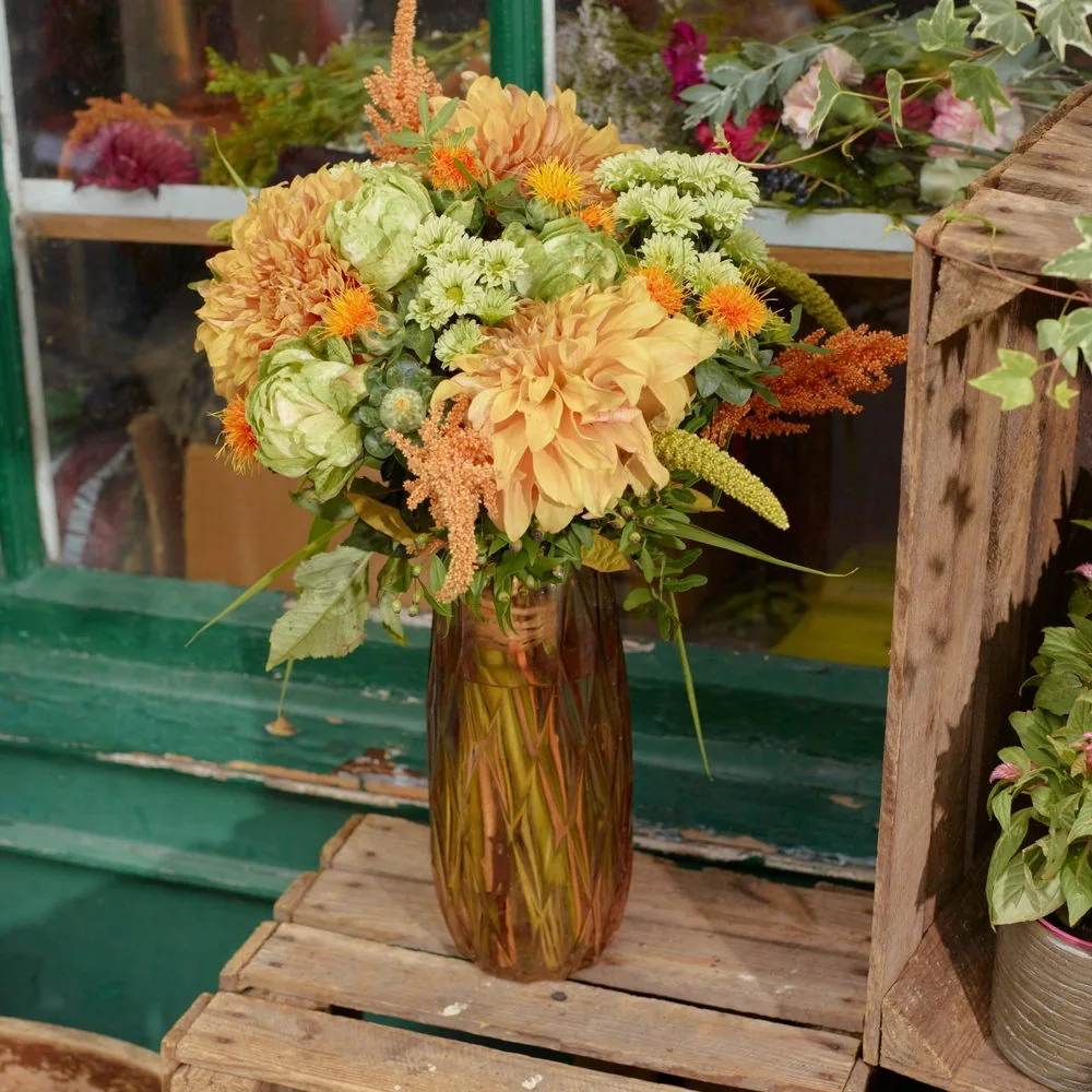 Bouquet orange et jaune dans un vase, devant la vitrine de la boutique