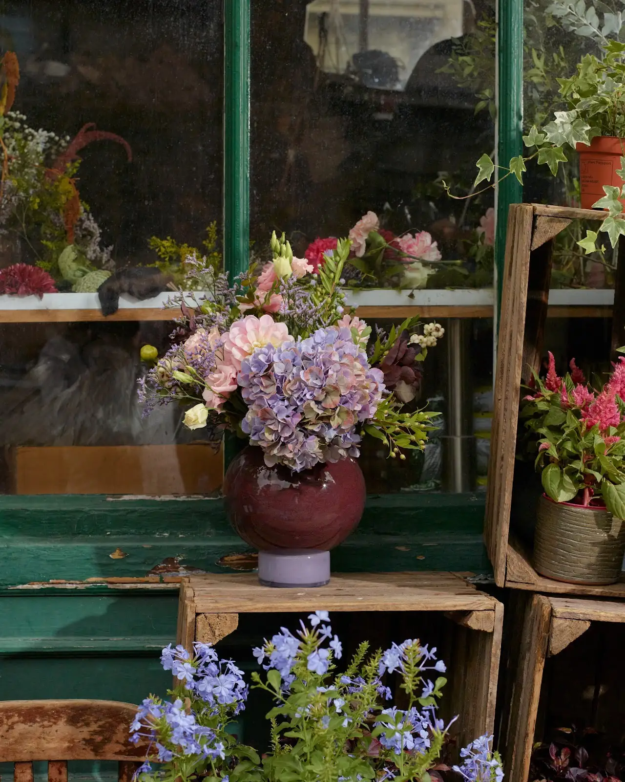Bouquet de fleurs bleues et roses posé sur des caisses en bois devant la boutique