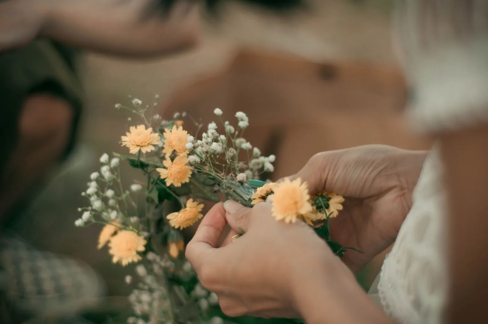 Mains qui assemblent un bouquet de fleurs jaunes et blanches, avec un léger flou sur la table en bois
