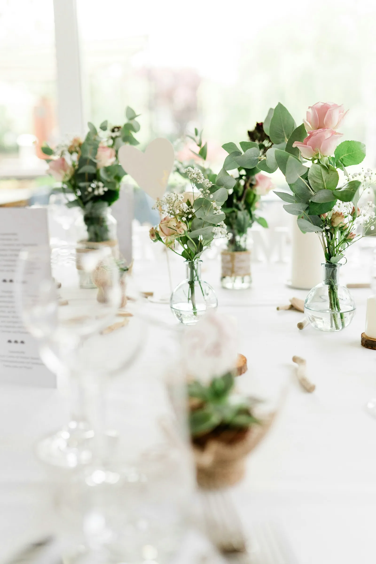 Plusieurs petits vases en verre avec des roses roses et blanches posés sur une table de mariage blanche