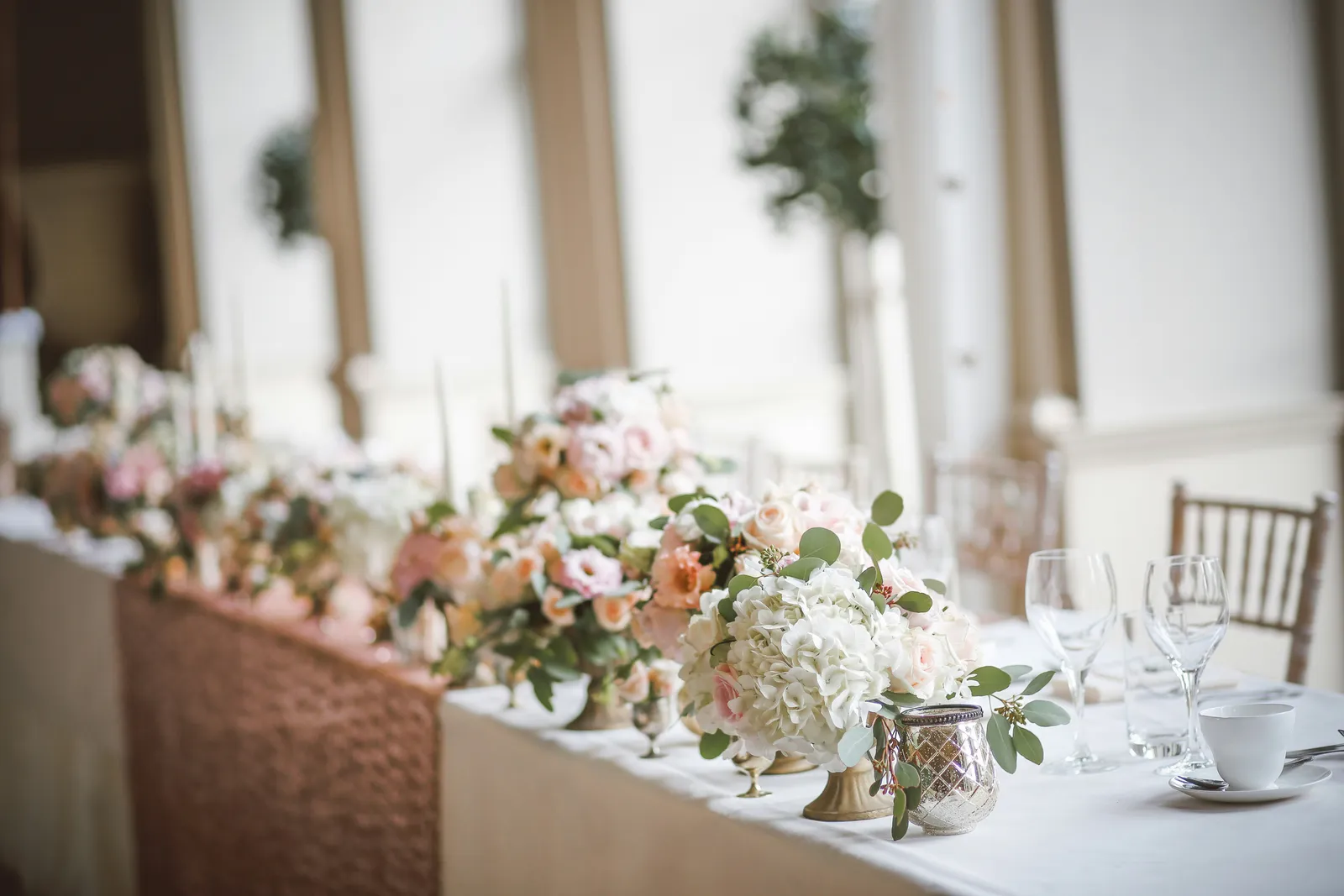 Table de réception de mariage dressée en intérieur, avec un centre de table fleuri bas et de la vaisselle
