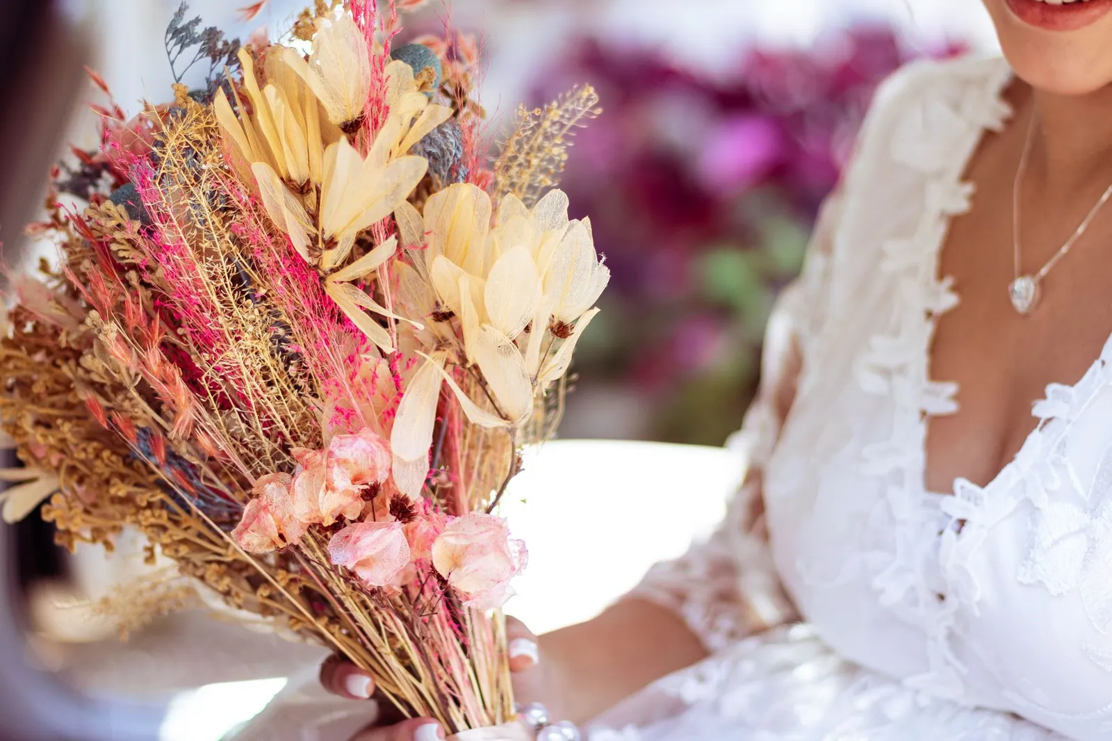 Bouquet de mariée séché aux couleurs passées, tenu par une mariée en robe blanche en dentelle