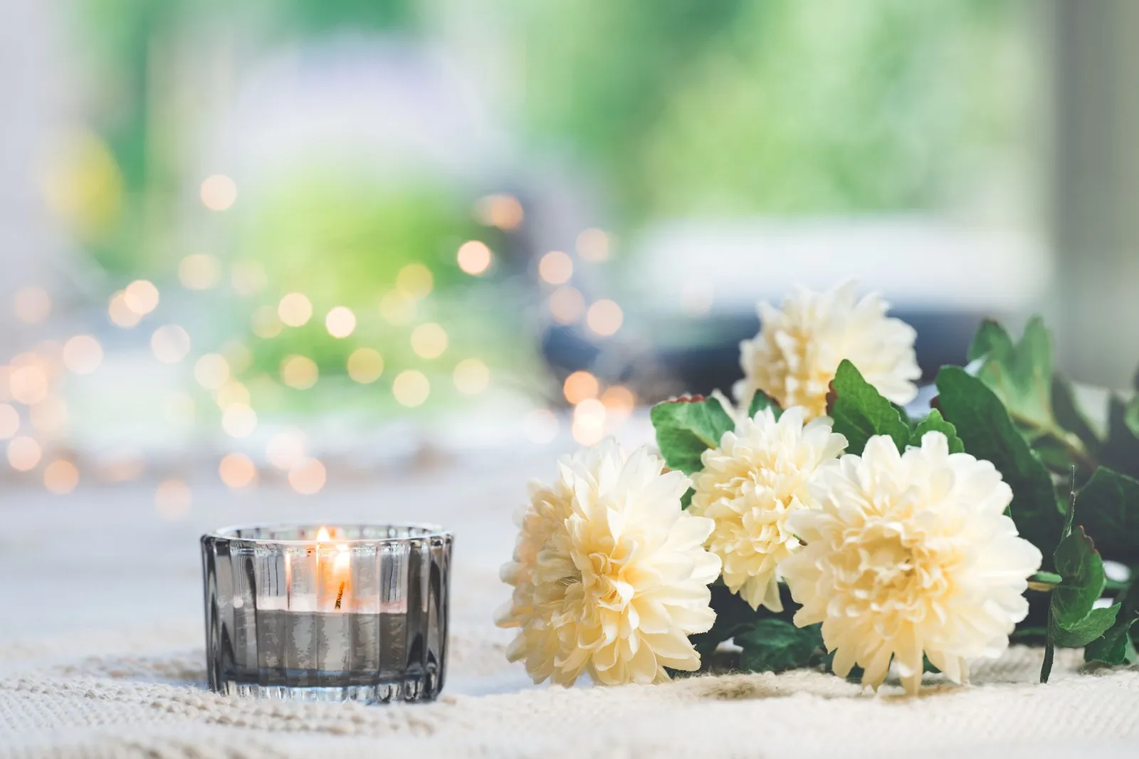 Bougie allumée et chrysanthèmes blancs sur une table, avec une lumière douce et un arrière-plan flou
