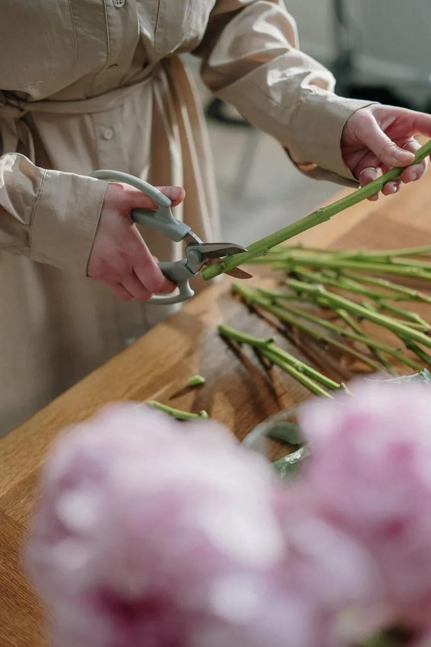 Des tiges de fleurs sont recoupées en biais au sécateur sur une table de travail