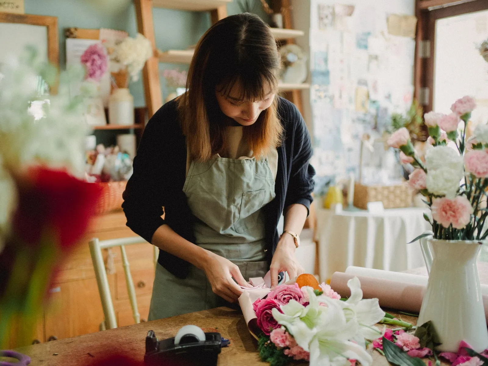 Fleuriste en tablier qui emballe un bouquet de roses et de lys blancs sur son plan de travail