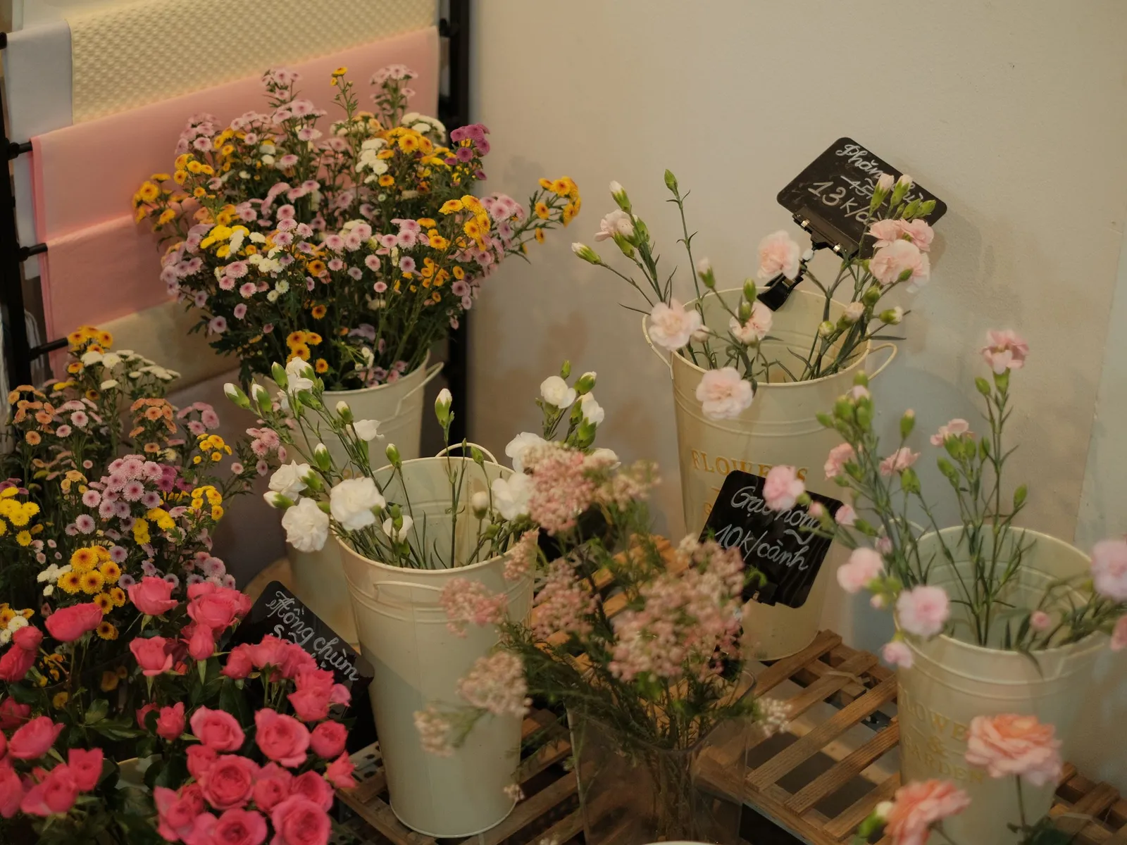 Œillets, marguerites et fleurs de saison dans des vases crème étiquetés à l'ardoise, dans une boutique de fleurs
