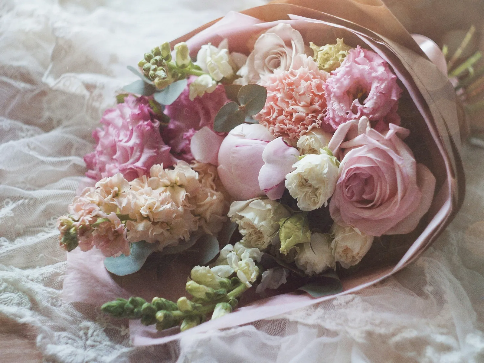 Petit bouquet de fleurs roses et blanches posé sur une surface en dentelle, dans des tons doux et pastel
