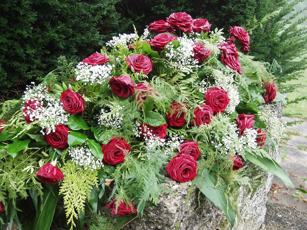 Composition funéraire de fleurs blanches posée au sol, avec roses blanches, petites fleurs et feuillage vert